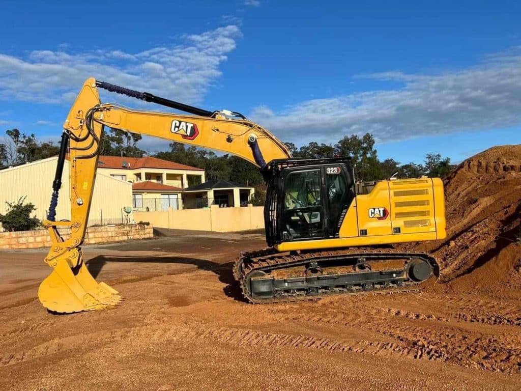 Full side view of the 2022 Caterpillar 323 Excavator with boom extended parked on red dirt stockpile at Western Truck Sales