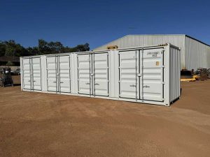 Side view of a white 40 foot shipping container on red dirt at Western Truck Sales yard with trees in the background