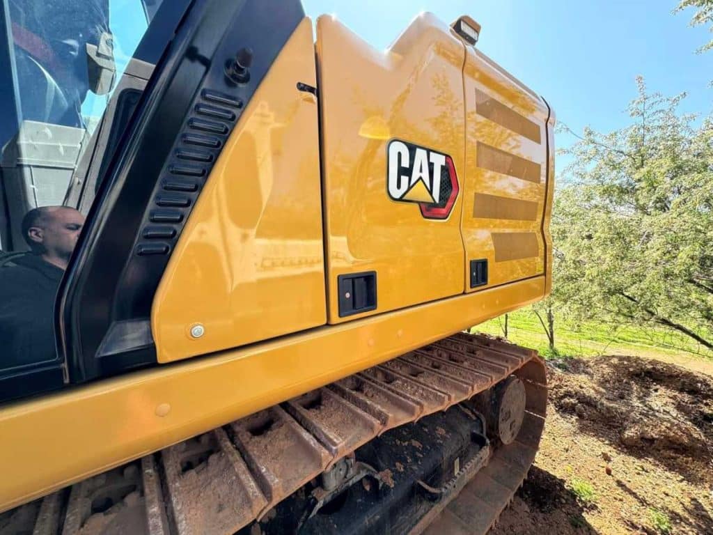 Rear quarter close up of the 2022 Caterpillar 323 Excavator showing CAT logo on counterweight and heavy-duty undercarriage tracks