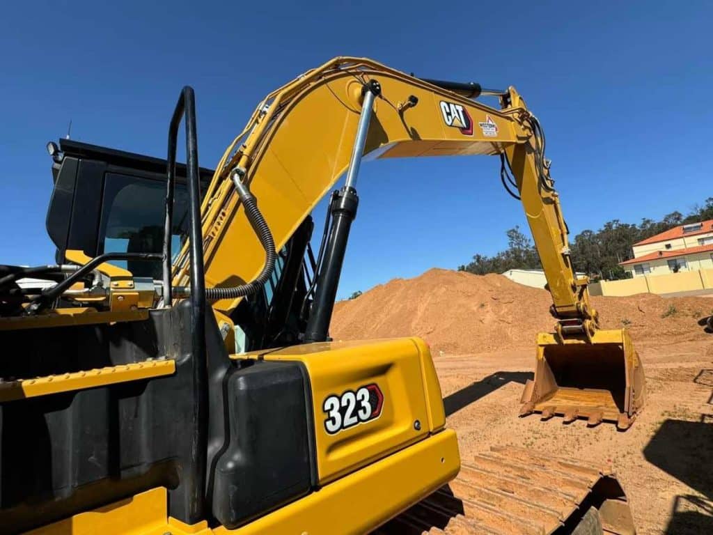 Rear quarter view of the 2022 Cat 323 Excavator showing 323 branding GP bucket attached and boom in working position on red dirt