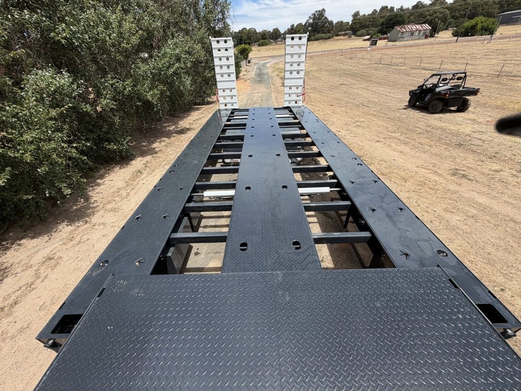 Rear view of FreightWest triaxle drop deck showing raised aluminium loading ramps in upright position