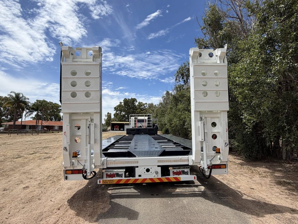 Rear angle of FreightWest HD triaxle drop deck highlighting the flat steel deck surface and triaxle wheel assembly
