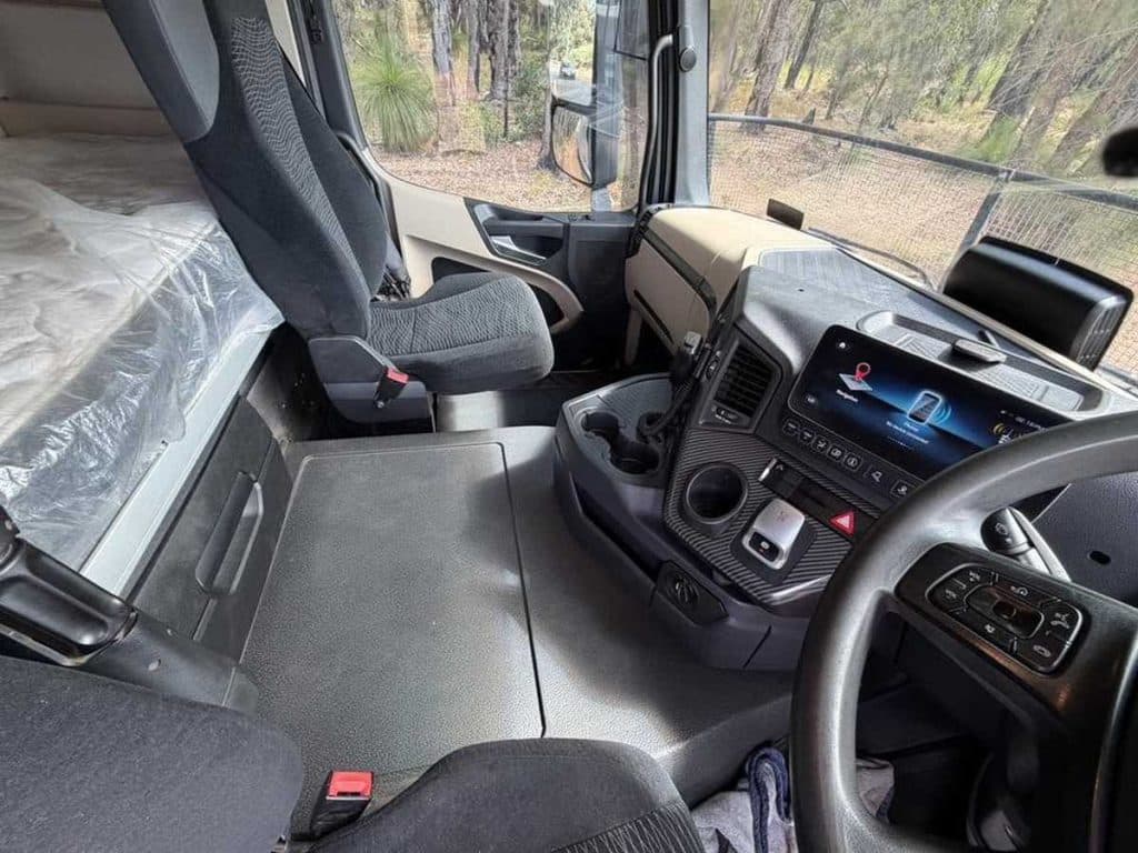 High-angle wide shot of the truck cabin interior, showing the passenger seat, floor mats, and main console