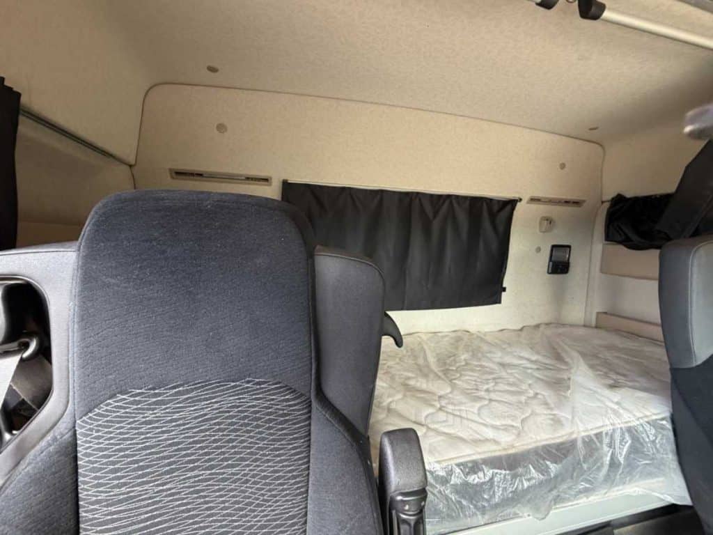 View of the rear sleeper cabin area inside the truck, showing the bunk bed mattress and black curtains.