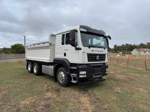 Front three-quarter view of the white Sinotruk Sitrak C7H tipper truck parked on a grassy field.