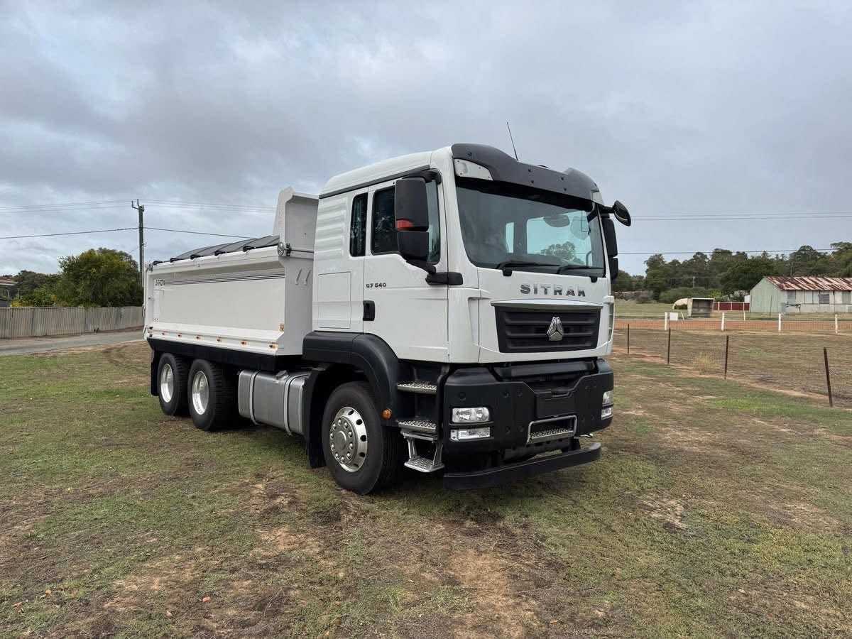 Front three-quarter view of the white Sinotruk Sitrak C7H tipper truck parked on a grassy field.