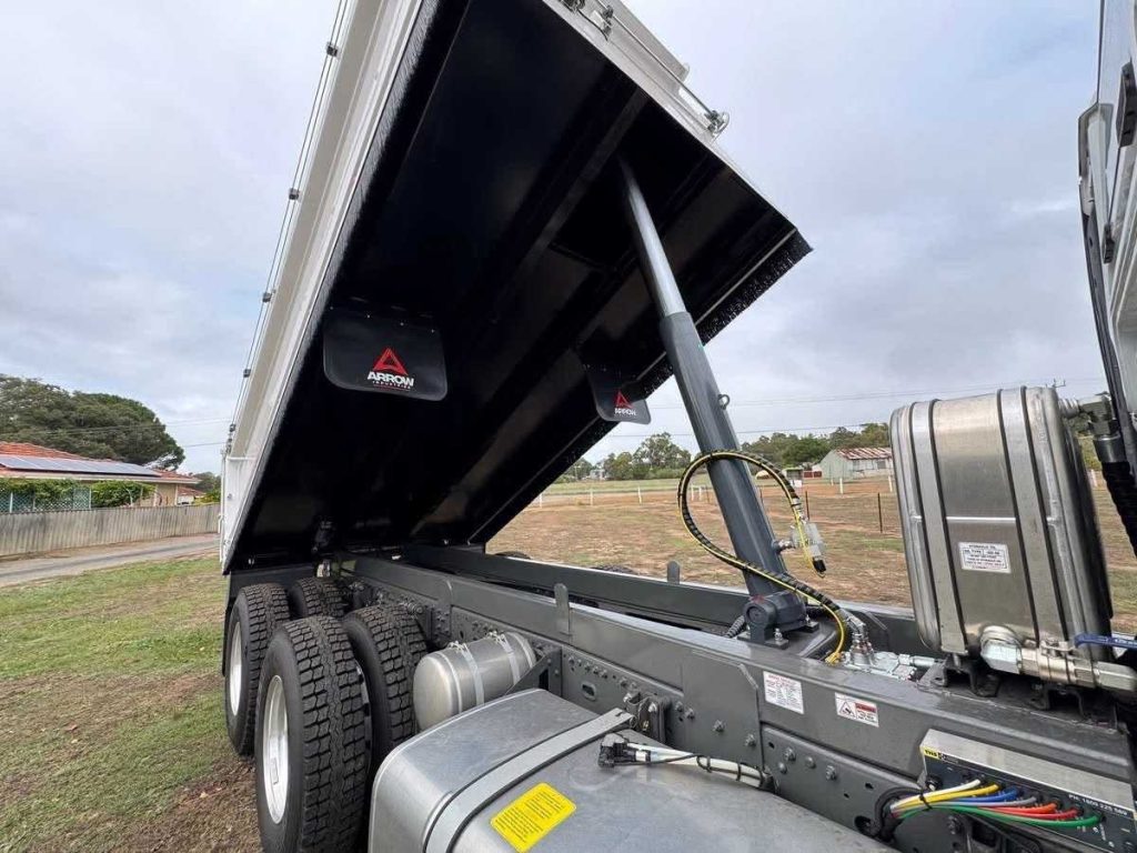 Detailed view looking up at the heavy-duty hydraulic lifting ram and undercarriage components beneath the raised tipper bed.