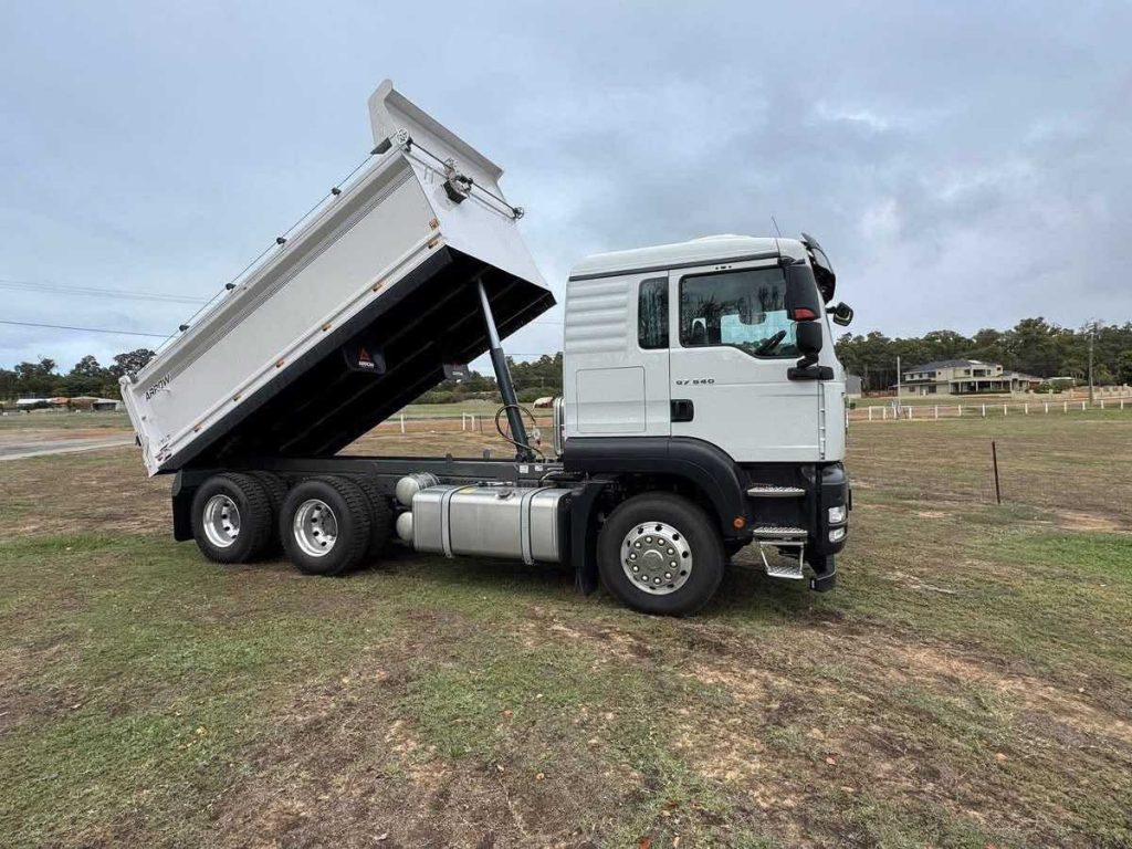 Side view of the white Sinotruk Sitrak C7H truck with its tipper tray fully lifted in the air.