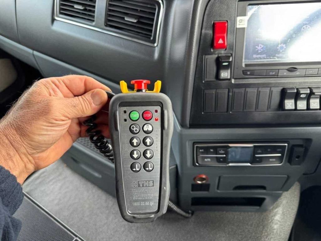 A close-up of a hand holding the wired electronic pendant remote control used to operate the tipper body.