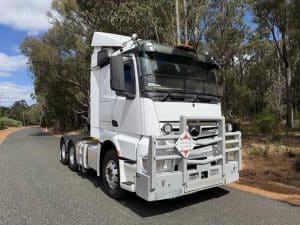 Front three-quarter view of a white Mercedes-Benz semi-truck cab with a silver bull bar, parked on a road